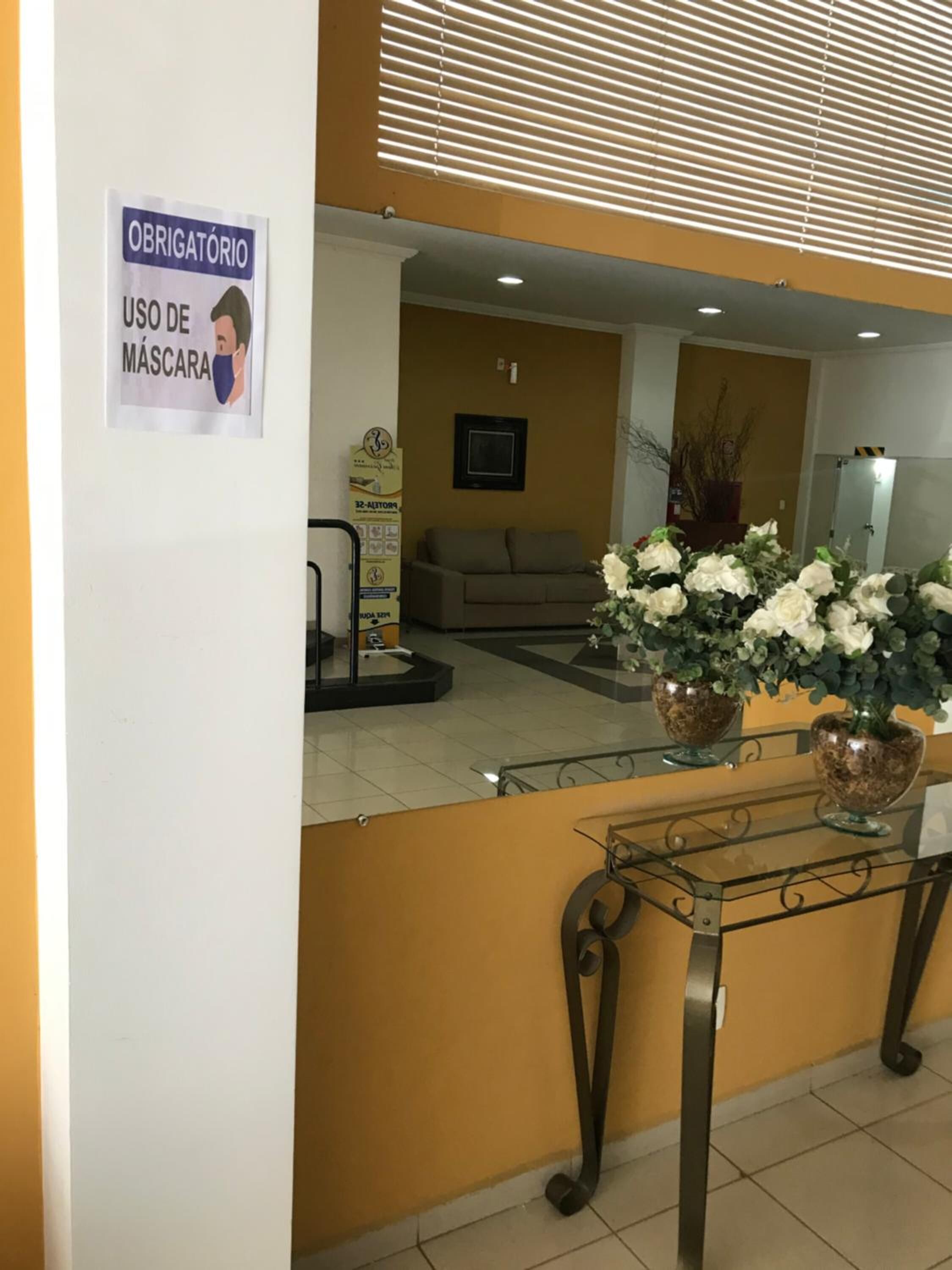 A reception area with a sign indicating mandatory mask usage, a sofa, a TV, and decorative plants.