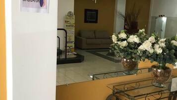 A reception area with a sign indicating mandatory mask usage, a sofa, a TV, and decorative plants.