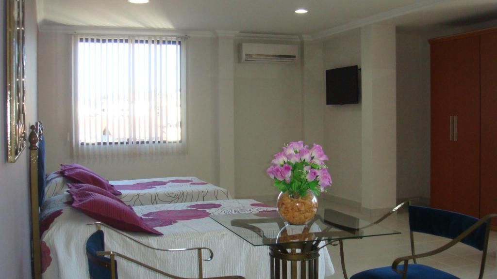 Ein Hotelzimmer mit einem Bett, einem Tisch mit Blumenvase, einem Sessel, einem Kleiderschrank und einem Fenster mit Jalousien.