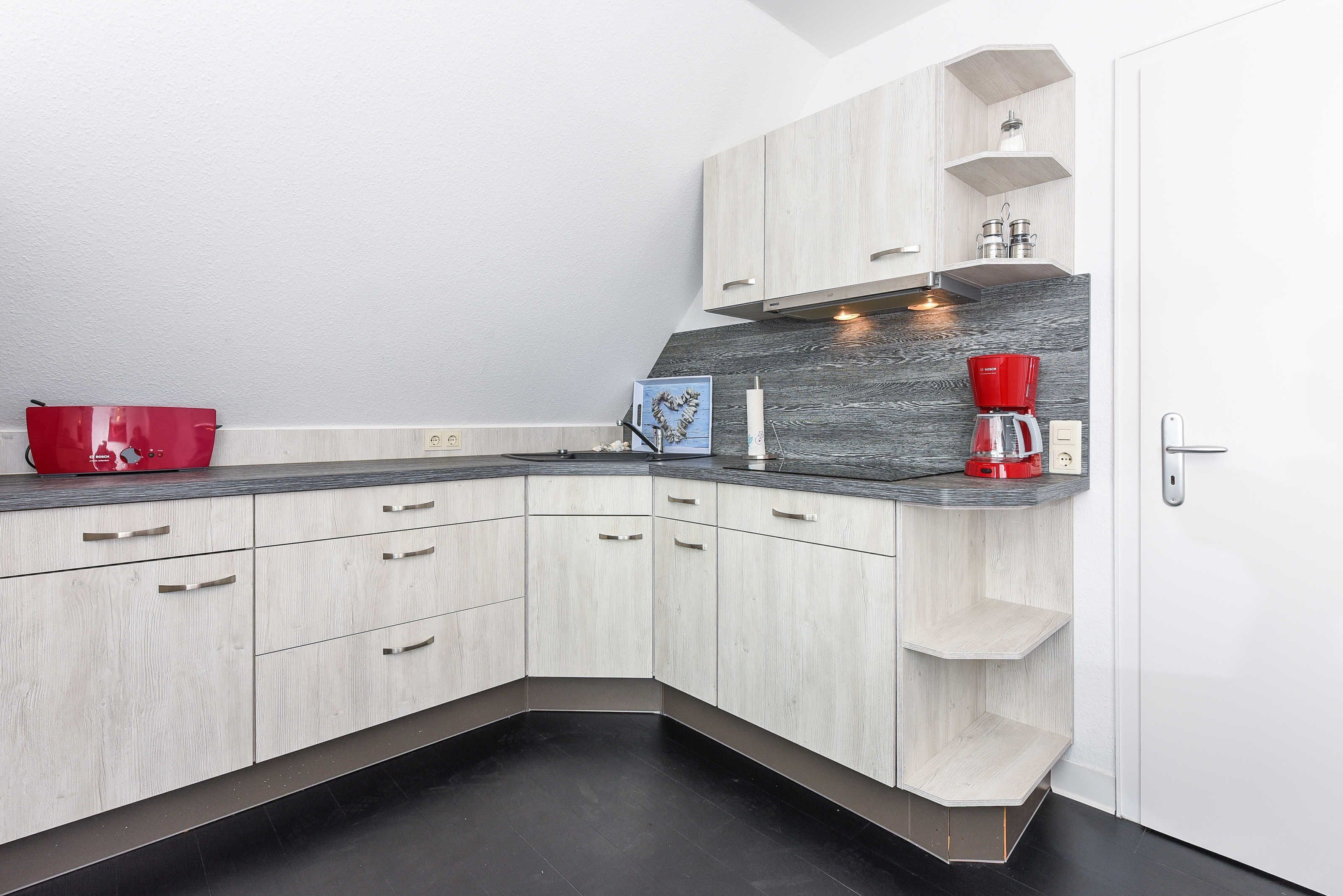 A modern kitchen with light wood cabinets, a dark countertop, and a built-in coffee maker.