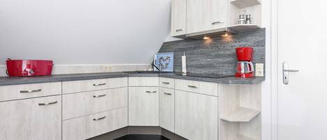 A modern kitchen with light wood cabinets, a dark countertop, and a built-in coffee maker.