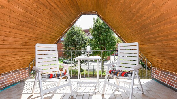 En overdækket terrasse med to hvide stole, et bord og udsigt til en have og huse i baggrunden.