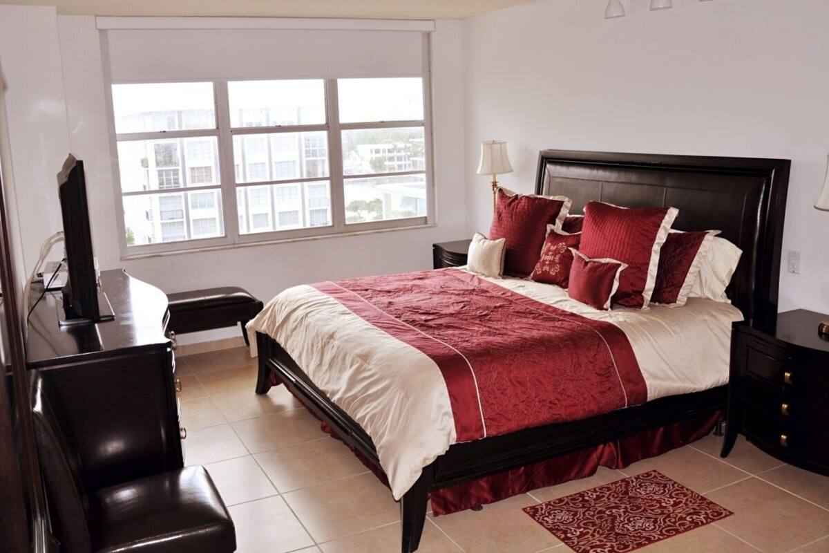 A bedroom with a bed, nightstands, a desk, and a window.
