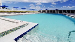 A clear blue swimming pool with a tiled edge, surrounded by lounge chairs and blue umbrellas. - Ocean Grand Residences (Miami Beach)