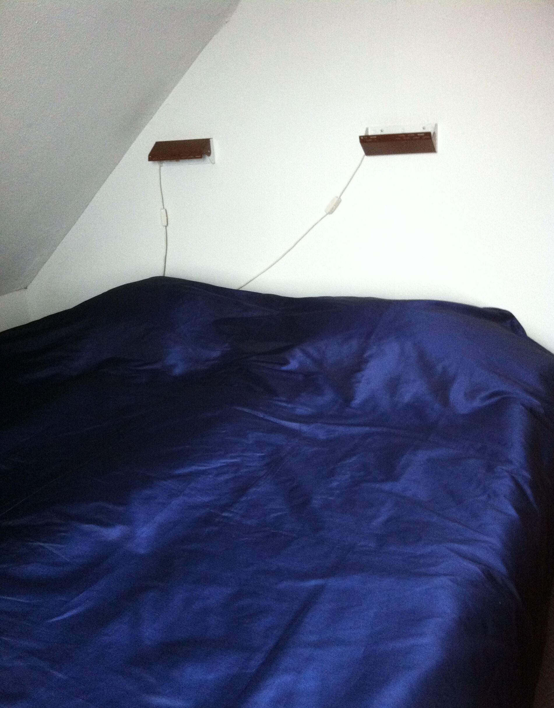 Ein Zimmer mit einer dunkelblauen Bettdecke, zwei Steckdosen an der Wand und einer geneigten Decke.