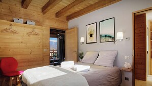 A bedroom with a wooden ceiling, a bed with white and grey bedding, a red chair, and two wall-mounted light fixtures. - Chalet Pajules - alpine holiday for 10 in Valmorel, sauna - OVO Network (Les Avanchers-Valmorel)