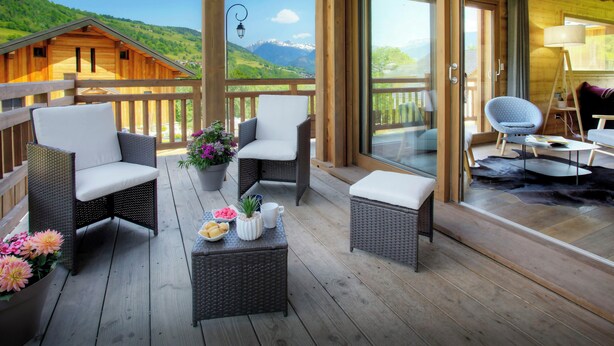 A wooden deck with wicker furniture, a potted plant, and a view of a mountain landscape. - Chalet Pajules - alpine holiday for 10 in Valmorel, sauna - OVO Network (Les Avanchers-Valmorel)