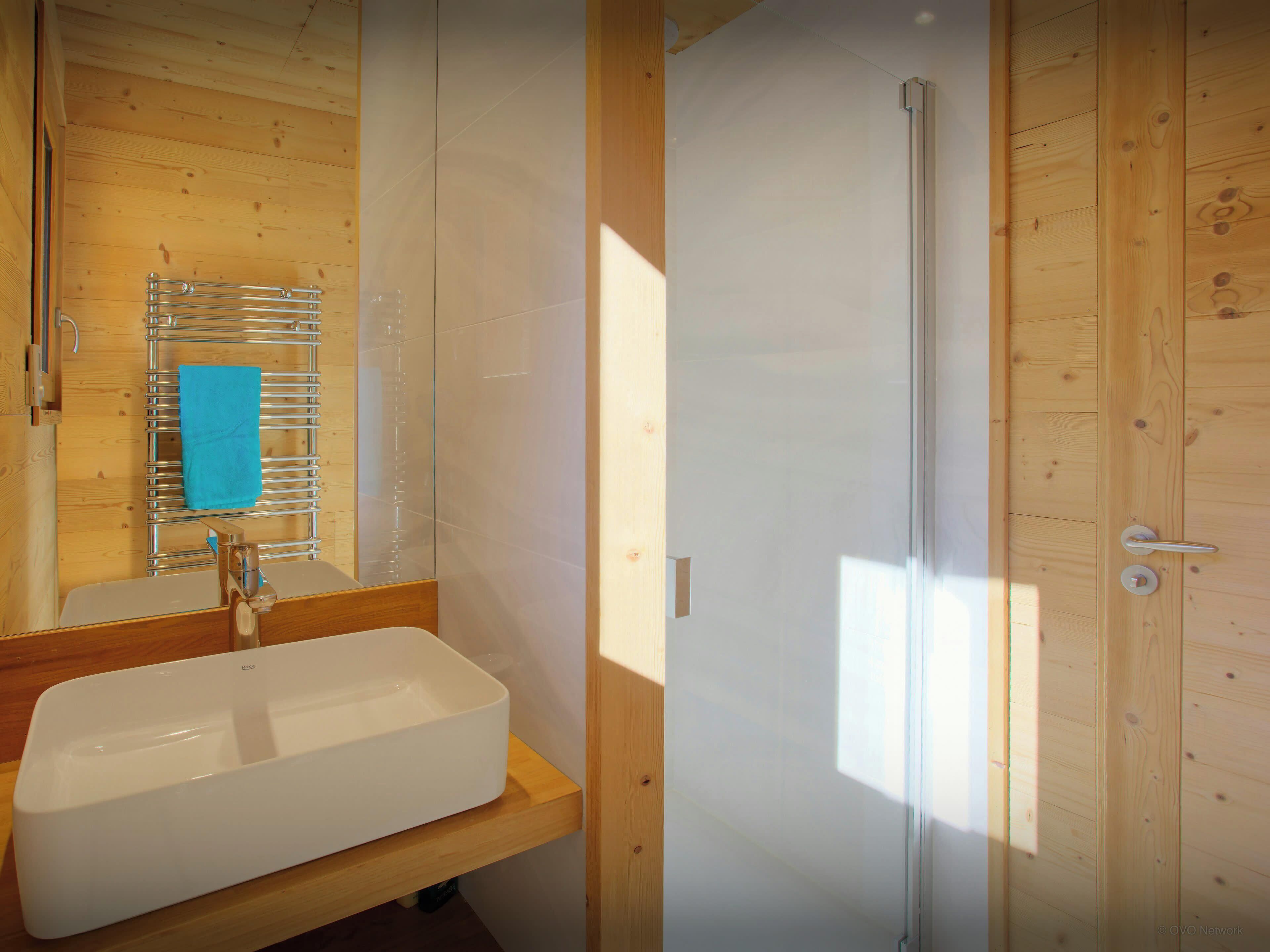 Un baño con lavamanos blanco, cabina de ducha de vidrio y paredes de madera.
