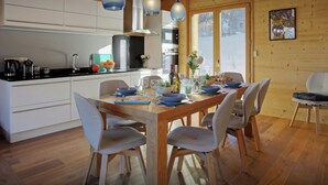 A modern kitchen with white cabinets, a wooden dining table set for six, and pendant lights. - Chalet Pajules - alpine holiday for 10 in Valmorel, sauna - OVO Network (Les Avanchers-Valmorel)