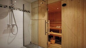 A modern bathroom with a glass-enclosed shower, wooden walls, and a visible sauna area with towels and a bucket. - Chalet Pajules - alpine holiday for 10 in Valmorel, sauna - OVO Network (Les Avanchers-Valmorel)