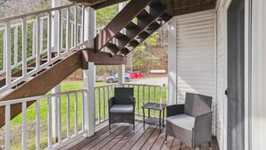 A wooden deck with a staircase leading to a covered area, two wicker chairs, and a small table.