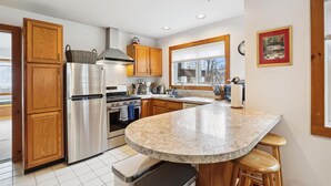 A modern kitchen with wooden cabinets, stainless steel appliances, a granite countertop, and a large window.