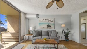 Un salon moderne avec un canapé gris, une table basse en bois et un tapis aux motifs tropicaux.