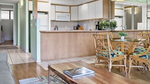 Une cuisine moderne avec des meubles blancs, un îlot central en bois et un coin repas doté de chaises en osier.