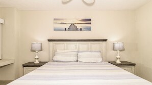Une chambre à coucher avec un grand lit, deux tables de chevet avec des lampes, une tête de lit et un tableau au mur.