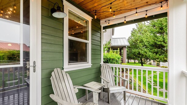 Une véranda avec deux fauteuils Adirondack, une petite table et une fenêtre décorée de guirlandes lumineuses.