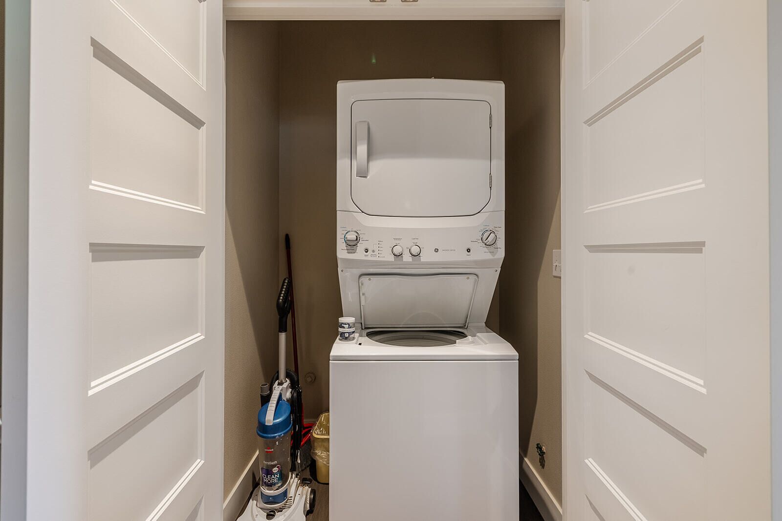 A compact laundry room with a front-loading washer and dryer, a vacuum cleaner, and a storage cabinet.
