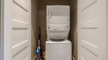A compact laundry room with a front-loading washer and dryer, a vacuum cleaner, and a storage cabinet.