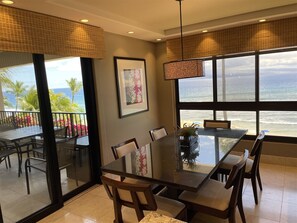 Un comedor con una mesa y sillas de vidrio, una lámpara colgante y vista al océano.