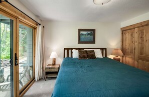 Un dormitorio con una cama grande, cabecera de madera, mesita de noche con lámpara y un cuadro en la pared.