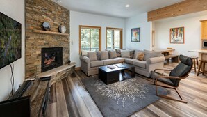 Una sala de estar moderna con chimenea de piedra, un sofá seccional, una mesa de centro y un televisor.