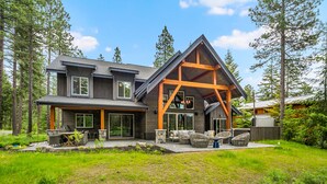 A modern two-story house with a large deck, surrounded by a forest.