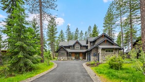 A large, two-story house with a stone facade, surrounded by tall pine trees.