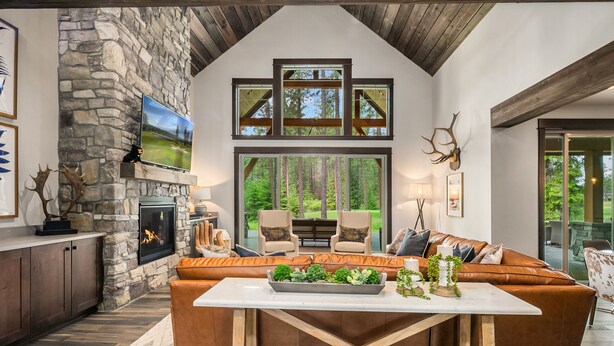 A spacious living area with a stone fireplace, leather sofa, and a large window overlooking a forest.