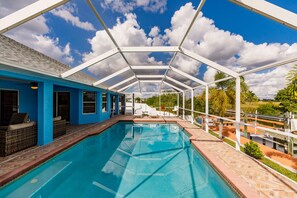 A pool area with a covered section, clear blue sky, and surrounding greenery.
