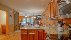 A spacious kitchen with wooden cabinets, granite countertops, and a central island with seating. - Loggers Run #7: 5 BR, 3.5 BA: Slope Side. Hot Tub, Overlooks Ski Trail! (Snowshoe)