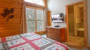A bedroom with a large window, a wooden dresser, a television, and a door leading to a bathroom. - Loggers Run #7: 5 BR, 3.5 BA: Slope Side. Hot Tub, Overlooks Ski Trail! (Snowshoe)