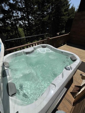 Un bain à remous sur une terrasse extérieure, avec une rambarde en bois et des arbres en arrière-plan.