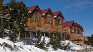 A multi-story wooden lodge with red roofs and balconies, surrounded by snow-covered trees. - Loggers Run #7: 5 BR, 3.5 BA: Slope Side. Hot Tub, Overlooks Ski Trail! (Snowshoe)