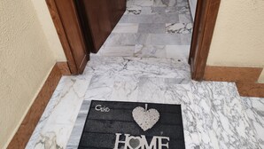 Un pasillo con suelo de mármol que conduce a una puerta. Un felpudo con la inscripción 'Geko HOME' se encuentra en la entrada.