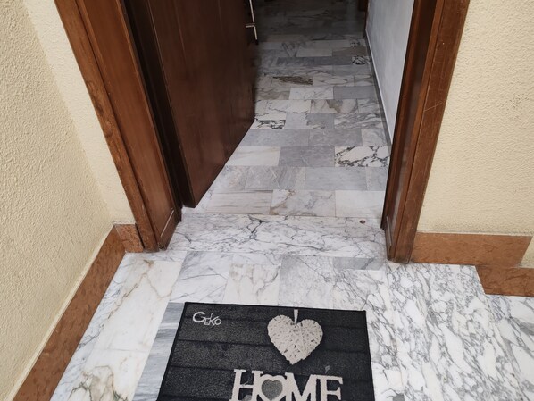 A hallway with a marble floor leading to a door. A doormat with the text "Geko HOME" is placed at the entrance.