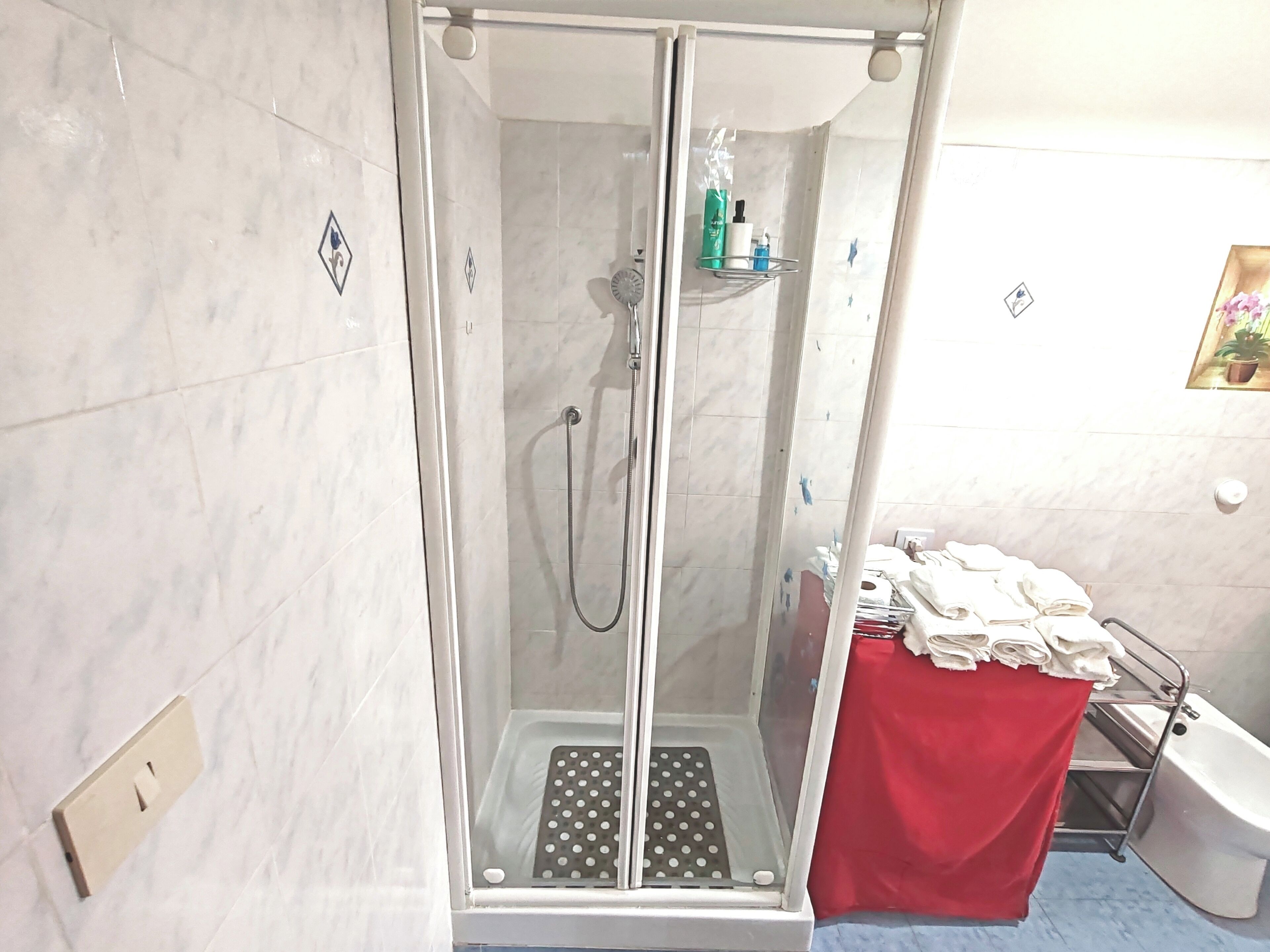 Un espacio de ducha con puerta de cristal, un toallero rojo y una bañera blanca.