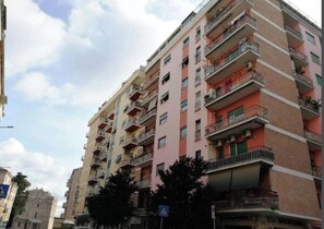 A multi-story residential building with balconies, a pedestrian crossing sign, and a blue traffic sign.