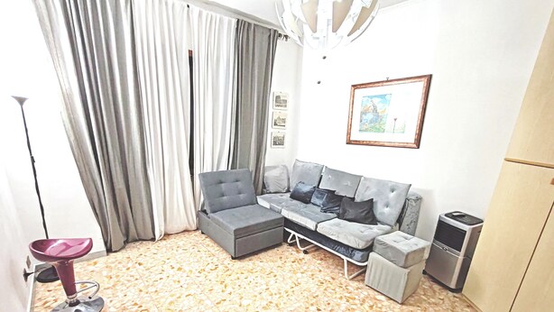 Una sala de estar con sofá, una mesita, una silla, un cubo de basura y un refrigerador.