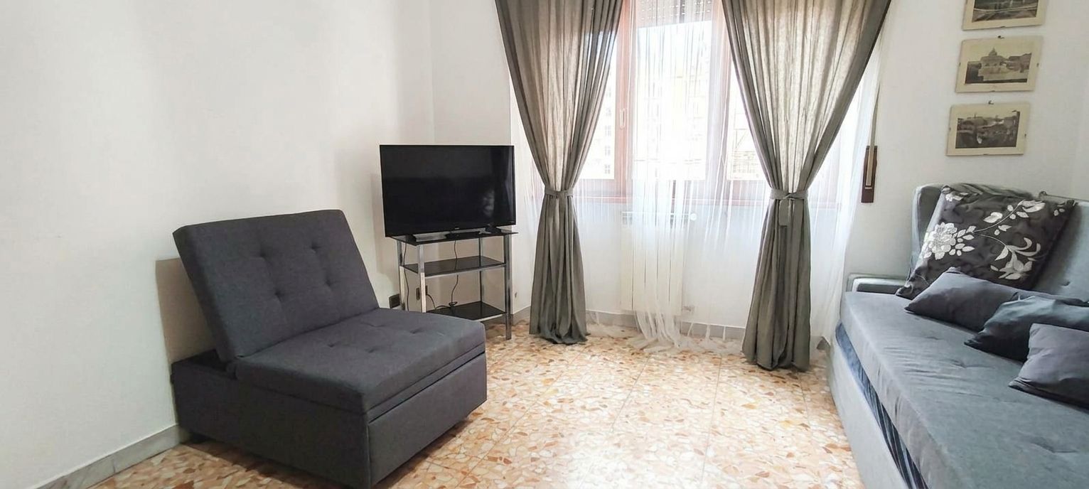 A living room with a sofa, a chair, a TV on a stand, and a window with curtains.