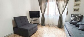 A living room with a sofa, a chair, a TV on a stand, and a window with curtains. - Apartment in the heart  of Rome free fast  wi fi (Roma)