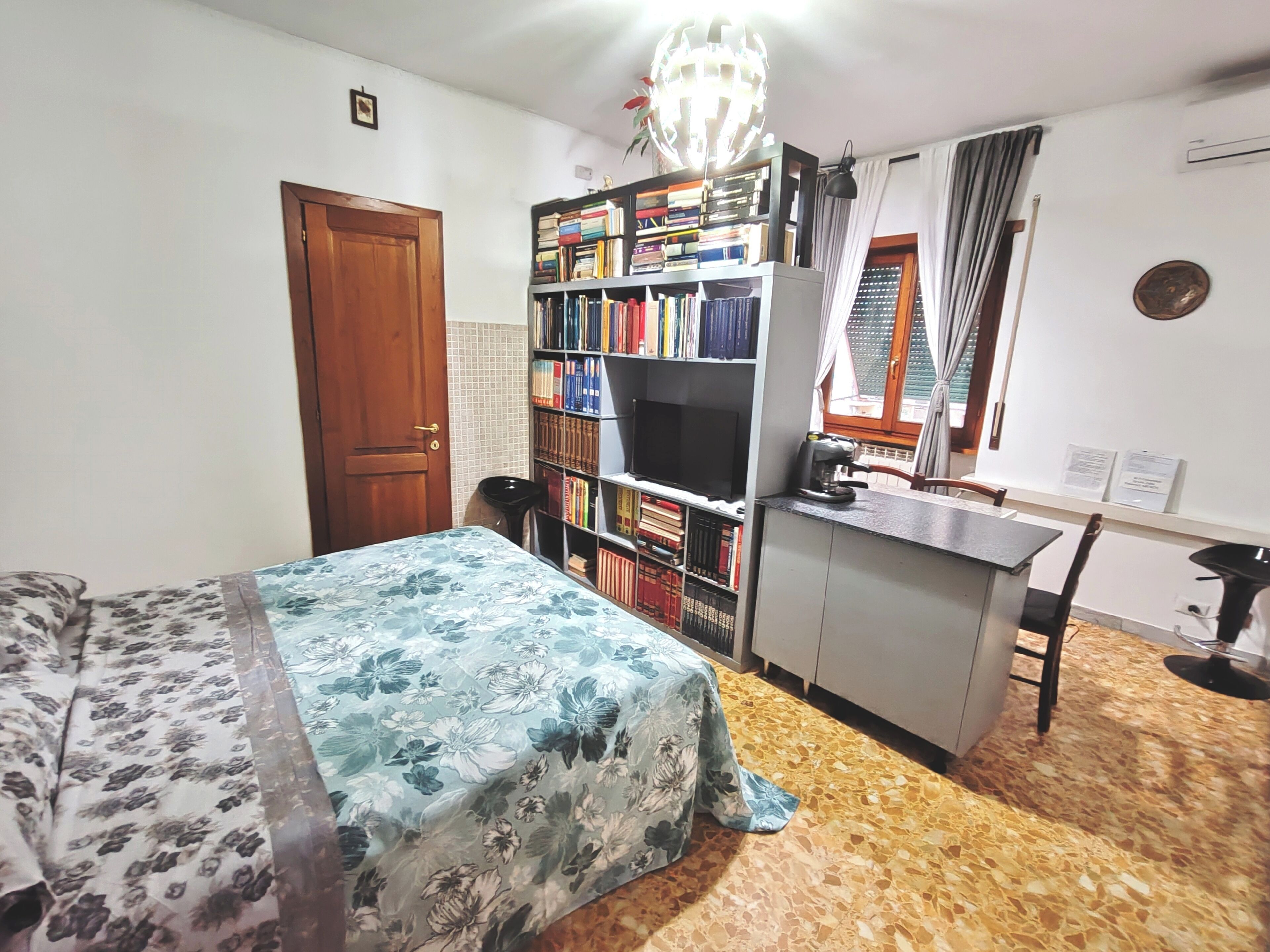 A bedroom with a bed, a bookshelf, a desk, and a window with curtains.