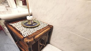 Un baño con tocador de madera, un lavabo, un mantel decorativo y un banco blanco.
