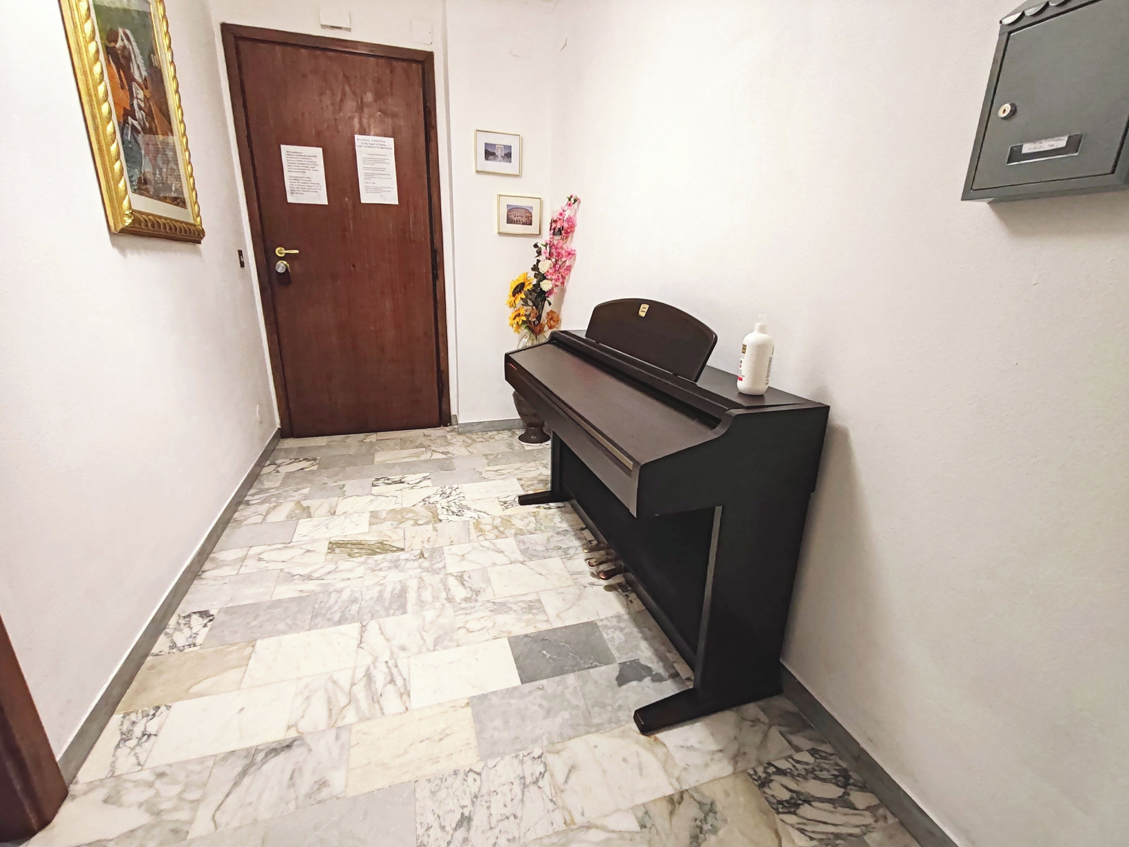 A hallway with a piano, a door with posted notices, and a patterned floor.