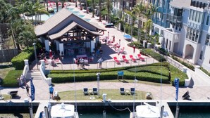 A marina with two white yachts docked, a covered seating area with tables and chairs, and a landscaped garden with palm trees.