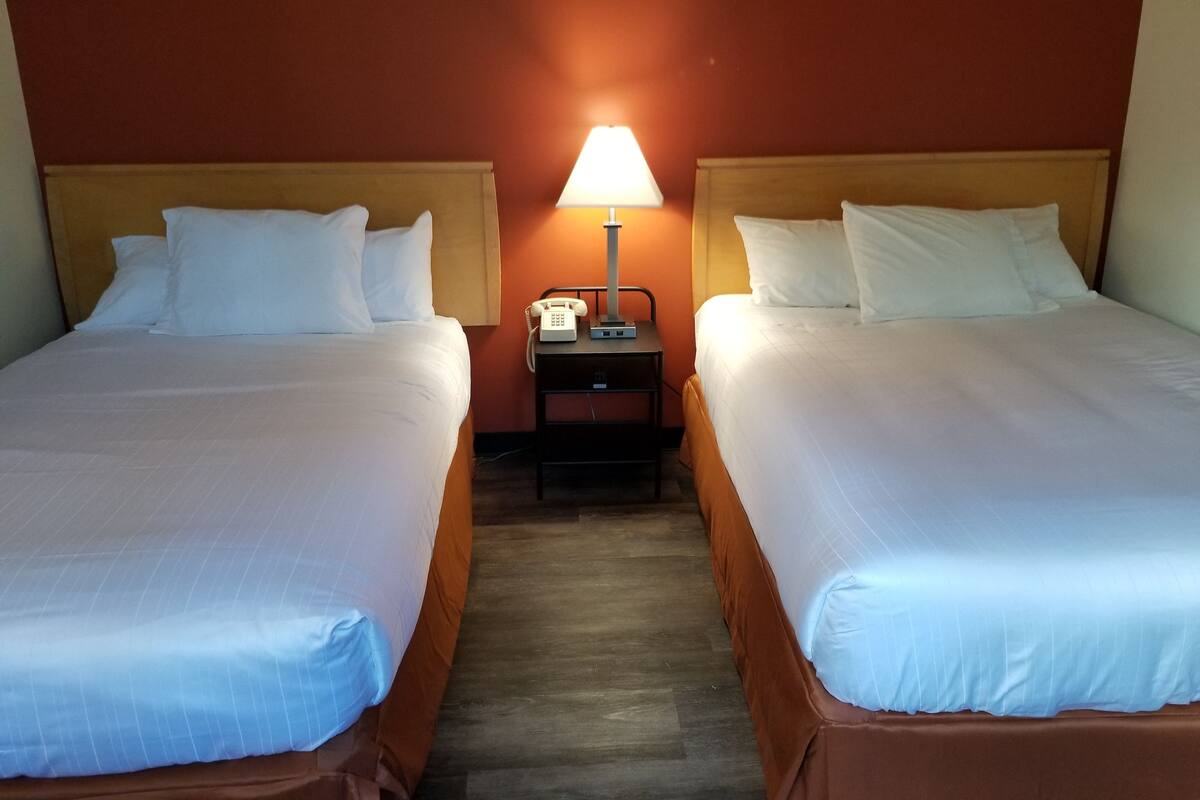 A hotel room with two beds, a nightstand with a lamp, and a telephone.