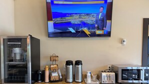Un comptoir de cuisine avec une machine à café, un grille-pain et un téléviseur qui affiche les prévisions météorologiques.
