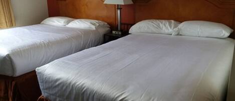 Dos camas individuales con sábanas blancas, un cabecero de madera y una mesita de noche con lámpara.