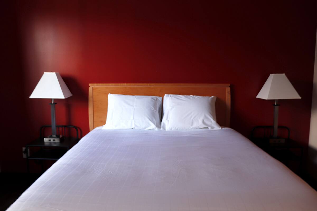 A neatly made bed with white linens, two bedside lamps, and a wooden headboard.