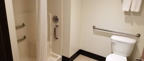 A bathroom with a shower, toilet, grab bars, and a towel rack.