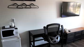 A modern office space with a desk, office chair, mounted TV, and a microwave on a small appliance.
